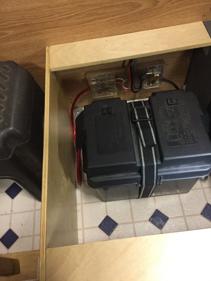 battery box strapped to floor with vent grate over turnbuckle access hole